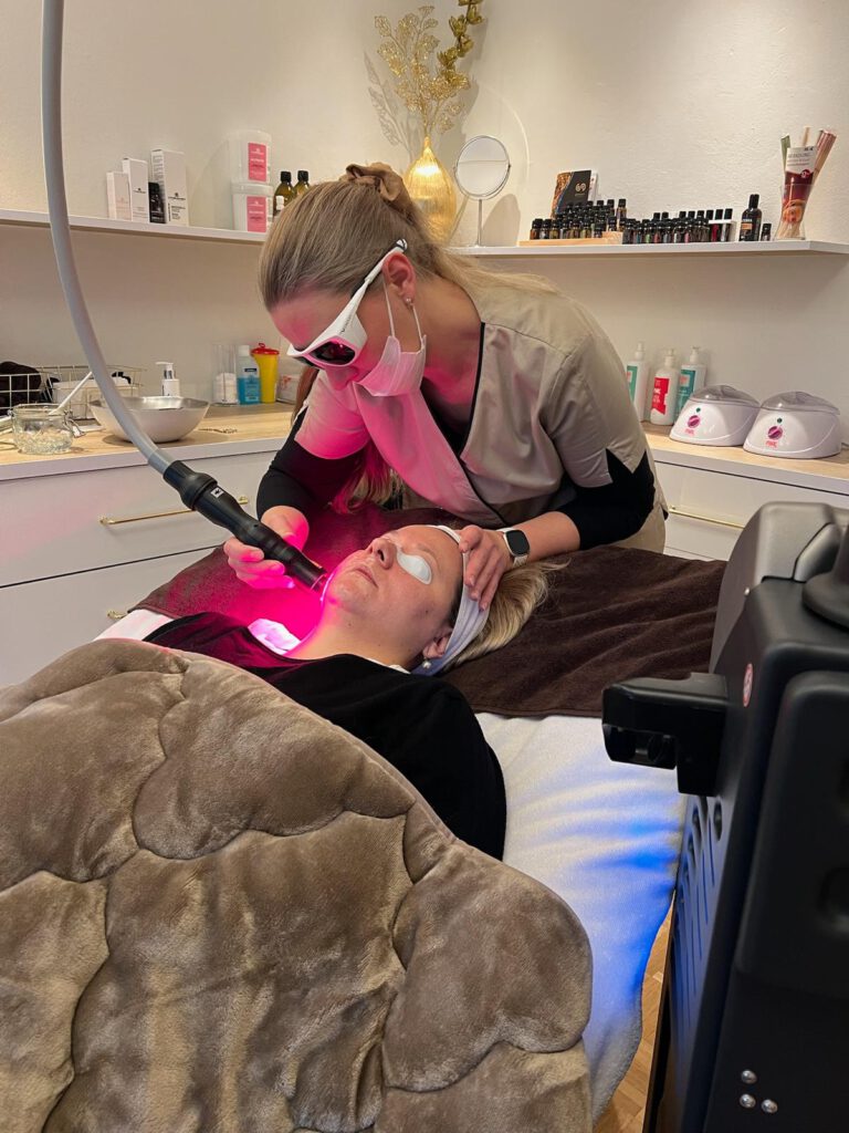 Das Bild zeigt die Kosmetikerin Kristina Bork-Menger im Studio bei der Gesichtsbehandlung einer Kundin mit einem Lasergerät.